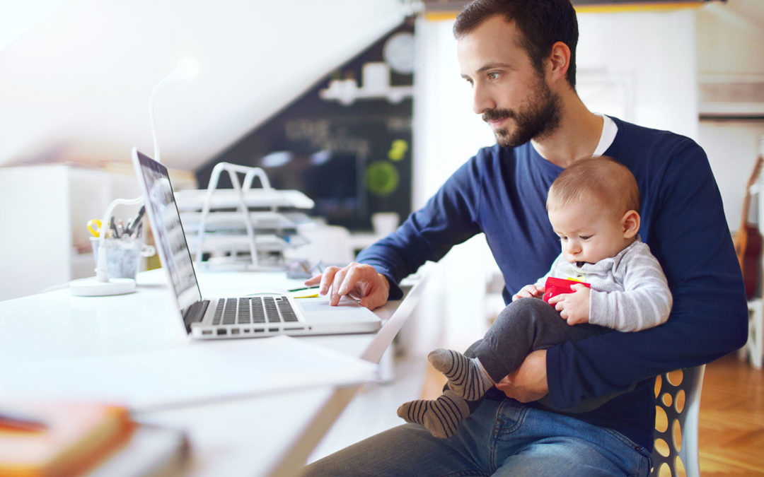 Father carrying baby son while working remote on his laptop